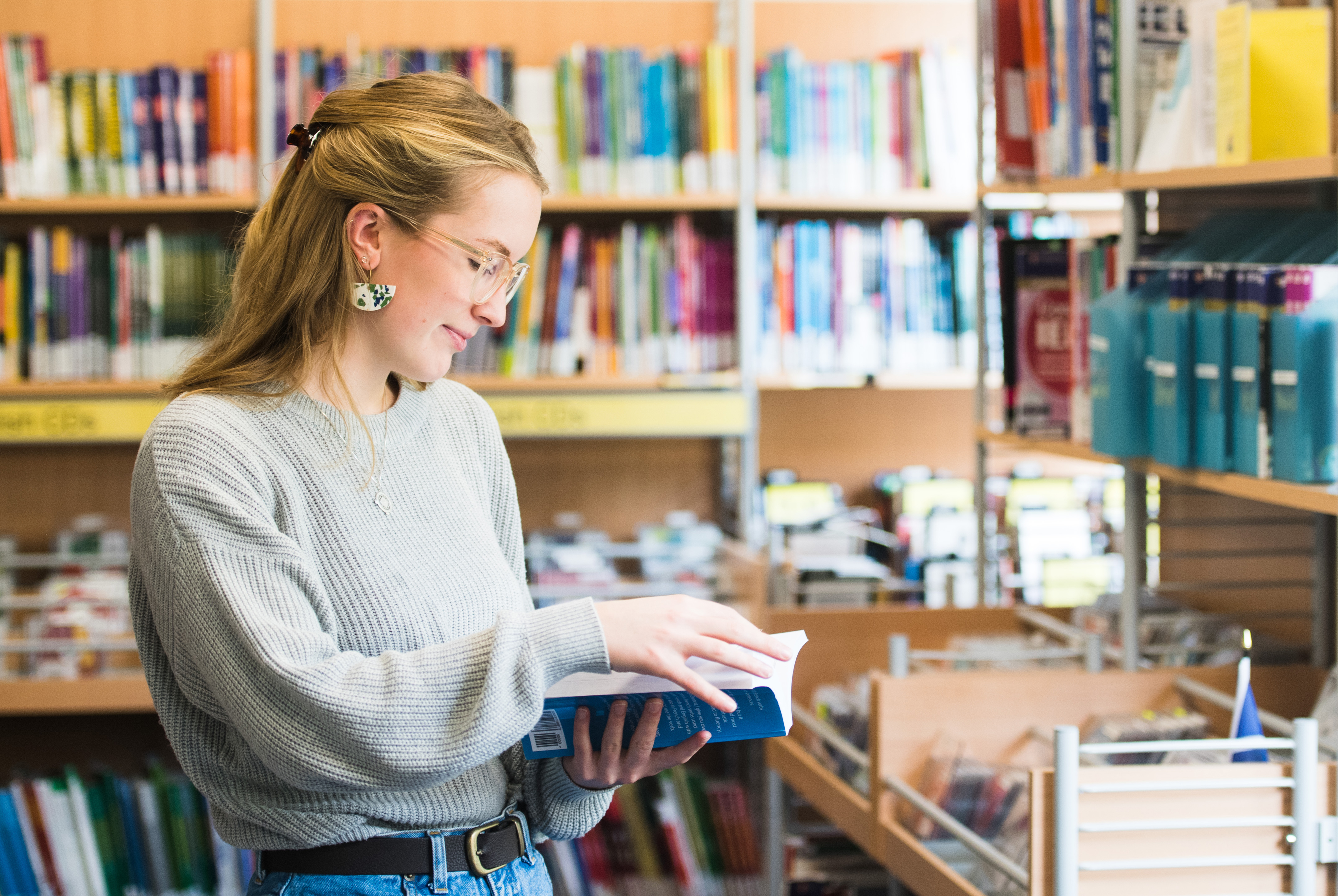 Female student standing reading a journal in the University library