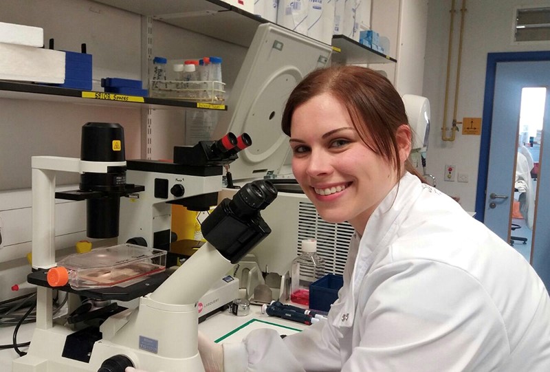 PhD student wearing lab coat in front of a microscope