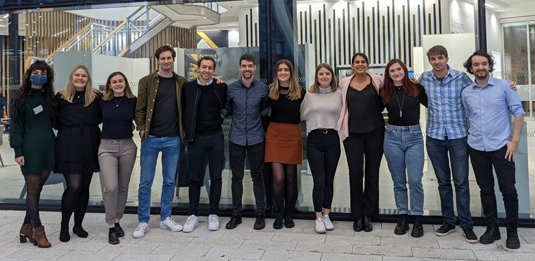 A group of PhD students stood in a line outside a UofG building